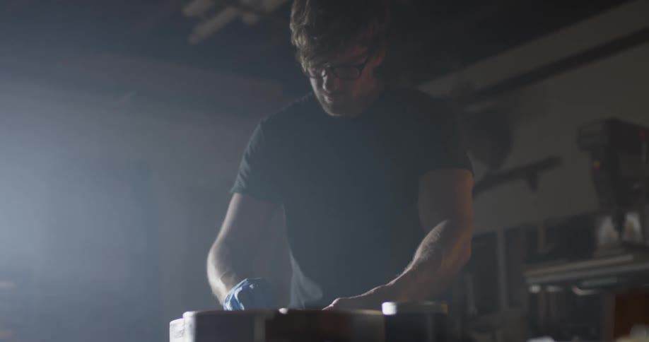 A man with glasses works on a guitar as he wears blue gloves