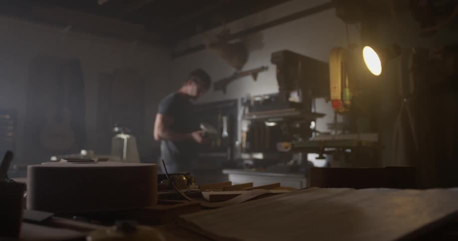 A man inspects something in his hands while he's in his workshop