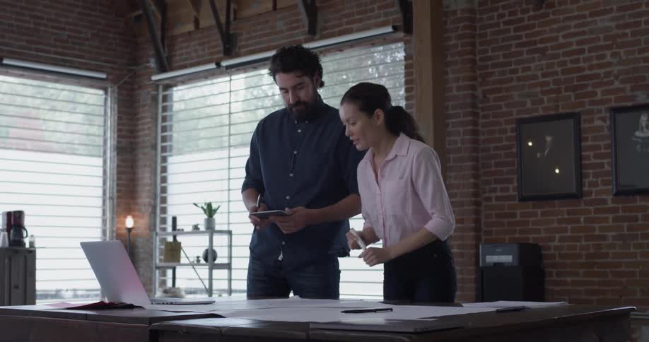 A woman writes something and shows the man standing next to her the computer screen