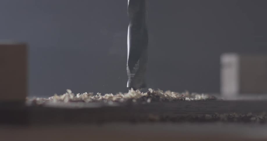 An electric drill bit being driven into wood kicking up sawdust