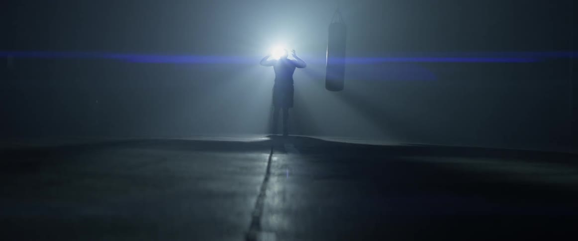 A man walks and rests his arms on his head in a dark gym
