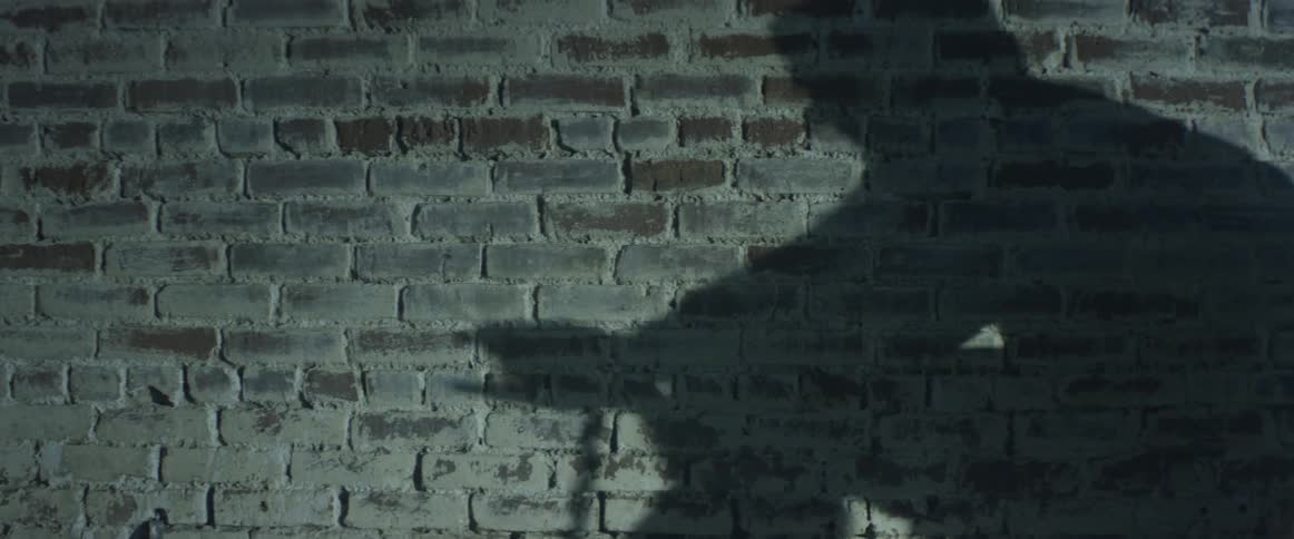 The shadow of a person unwrapping cloth from their hands shows on a brick wall