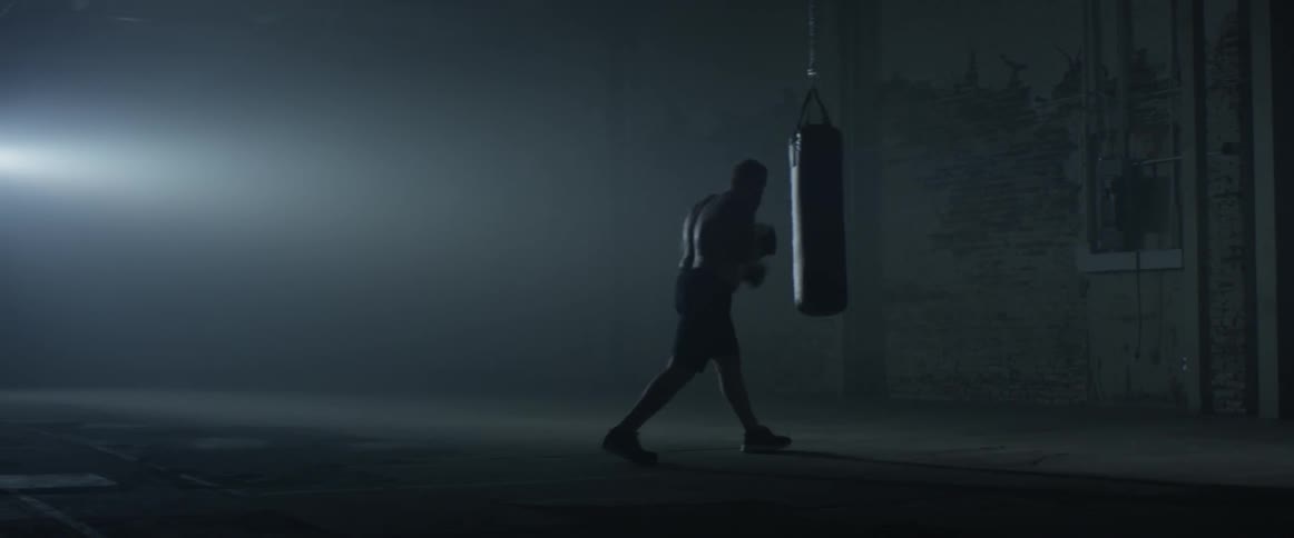 A man punches a punching bag in a dark gym