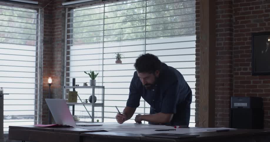 A man working on a laptop in a brightly lit room full of brick and windows