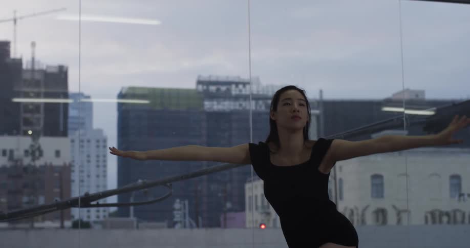 A woman dances with large glass windows behind her