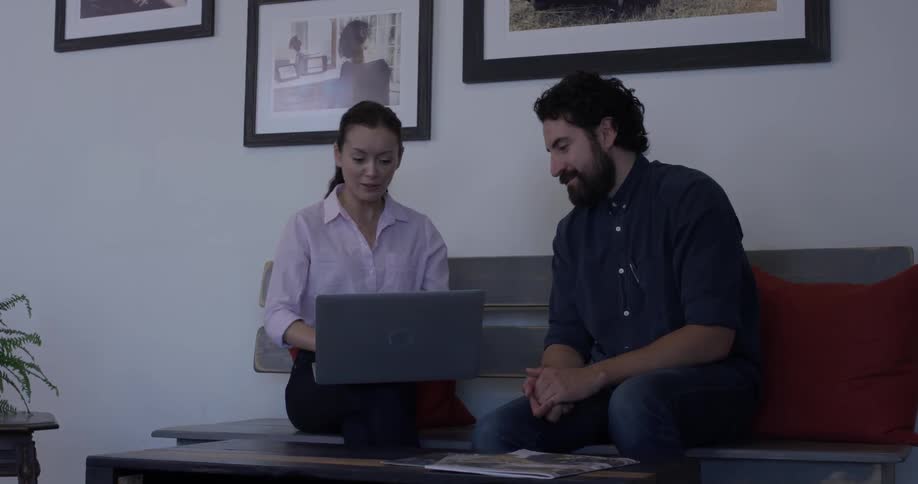 A man passes a laptop to a woman while they are talking
