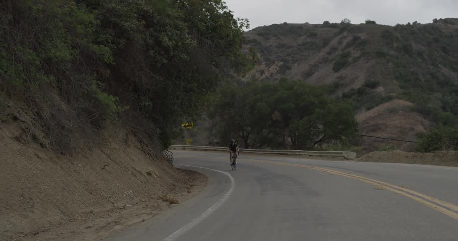 A man rides a bike down a curvy highway in the mountains