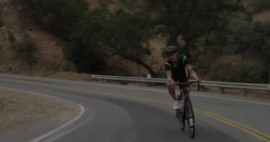 A man rides a bike along a winding mountain road at dusk