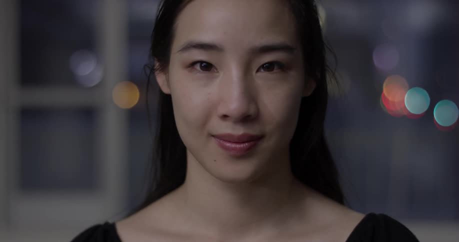 A woman inside a room blinks and looks up at the camera then smiles