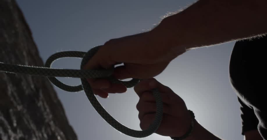 Person ties a rope on the side of a cliff on a sunny day