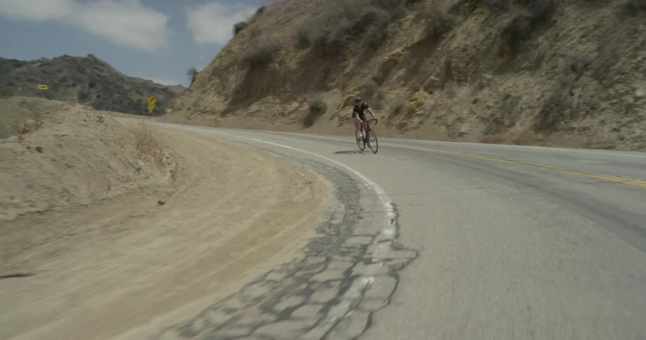 A man rides a bicycle around a mountain road turn