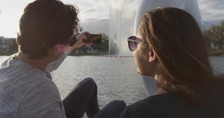 A man and woman taking a photo of a fountain while riding on a pedal boat