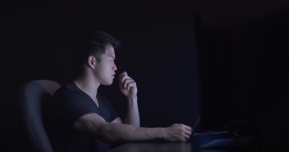 A man is focused on monitors and biting his finger