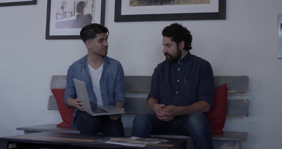 Two men sitting on a bench looking at a laptop