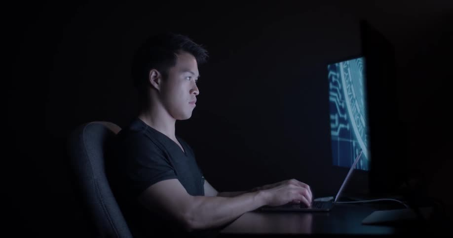 Man types on keyboard while sitting at desk and facing a monitor