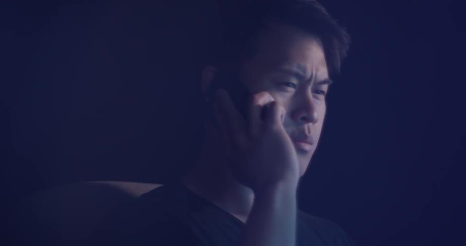 Man in a dark room talks on his cell phone while staring at something