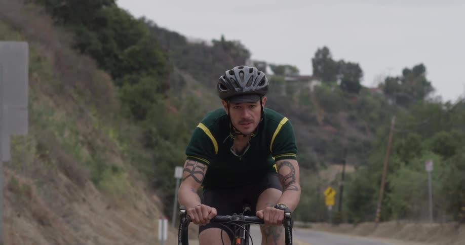 Man pedals a bike down a tree lined hilly road