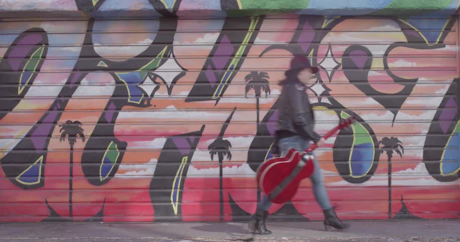 A woman carrying a guitar in front of a painted wall