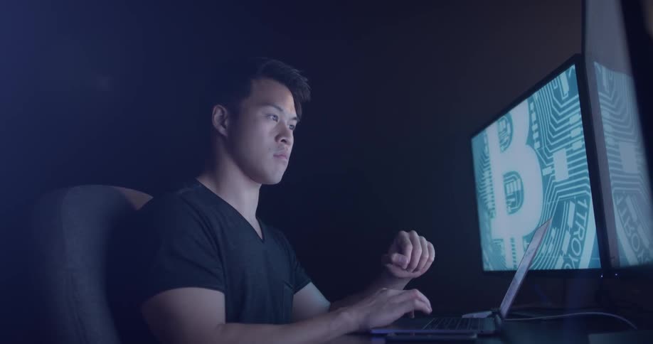 A man working on a laptop with large screens behind it