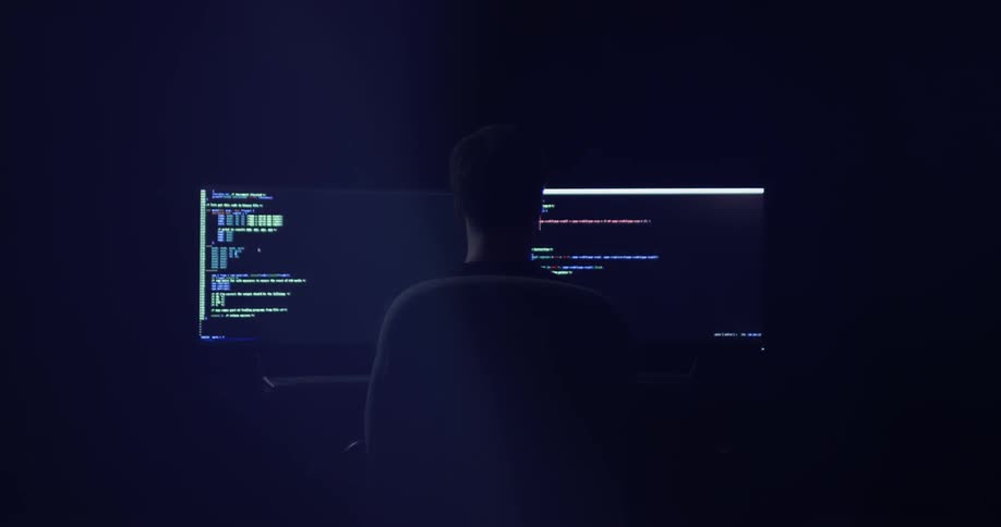 A person sitting at a desk glancing between two large monitors
