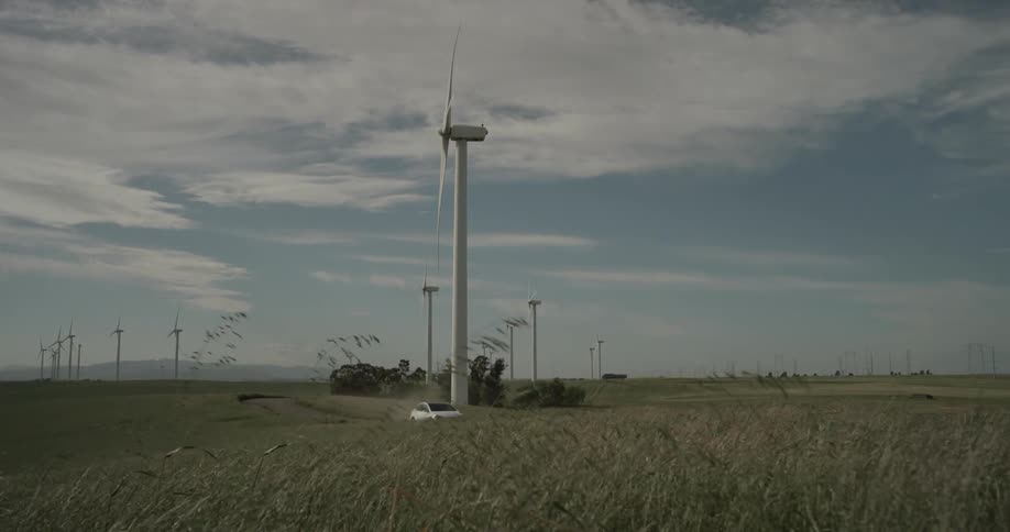 A car driving past a rotating windmill in a field