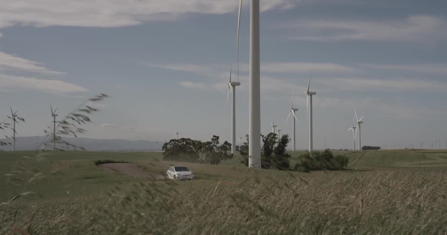 Man Driving Electric Car Through Wind Farm