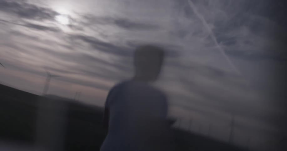 Window reflects man standing in field at a wind farm