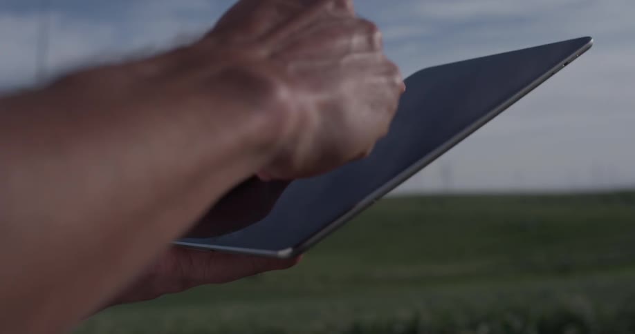 A man's hands work on a tablet outside in front of wind turbines