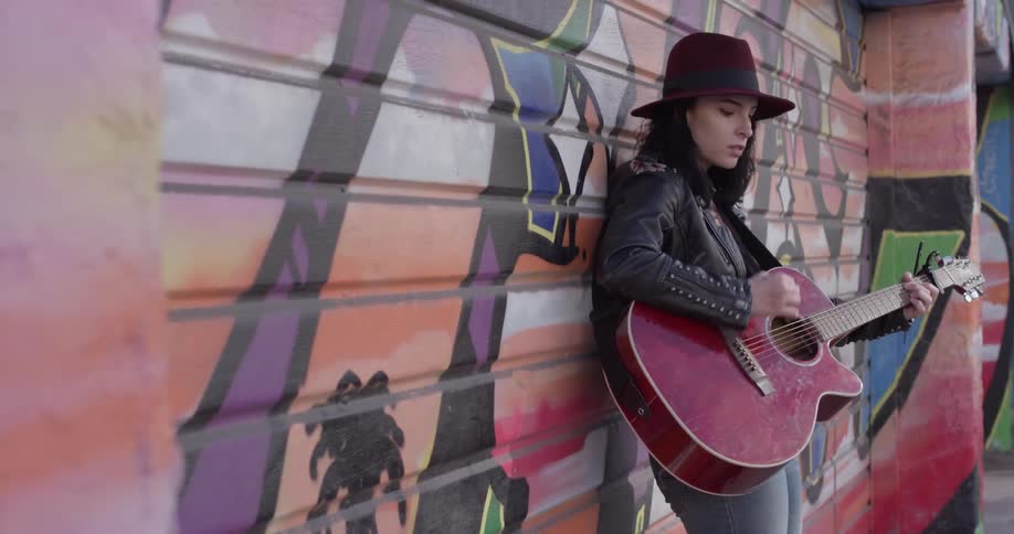 A woman standing next to a mural playing a guitar
