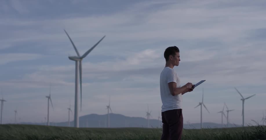 Man stands in field with windmills typing on a tablet
