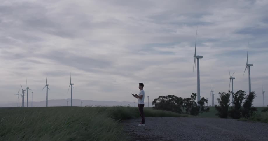 A man stands before windmills and uses a tablet