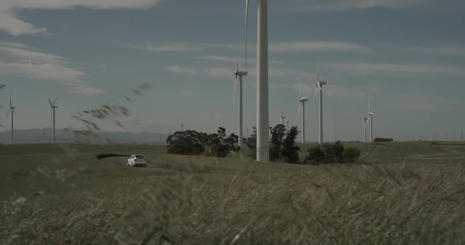 A car drives past tall wind turbines on a secluded road