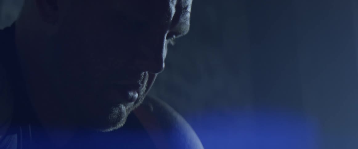 A bright light shines on a man with a solemn face