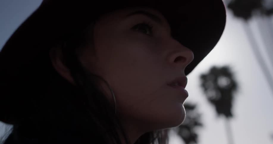Woman with dark hair and hat walks along a palm lined street