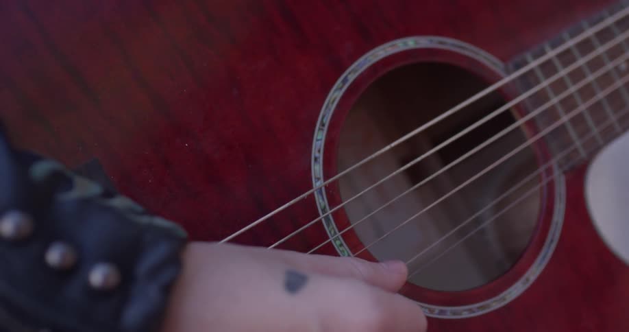Person plucks guitar strings with their thumb