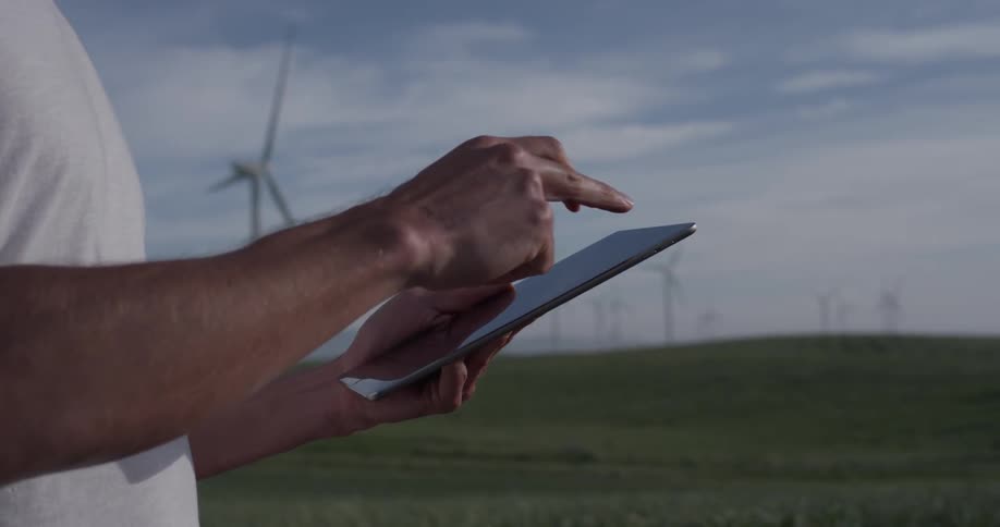 A person that is typing on a tablet near some windmills