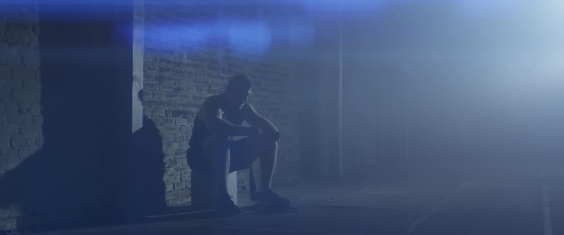 Man sits on a block next to a brick wall wrapping his wrist
