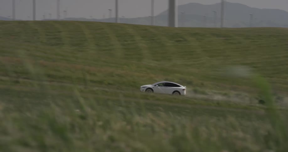 A white car driving up a dirt road next to windmills