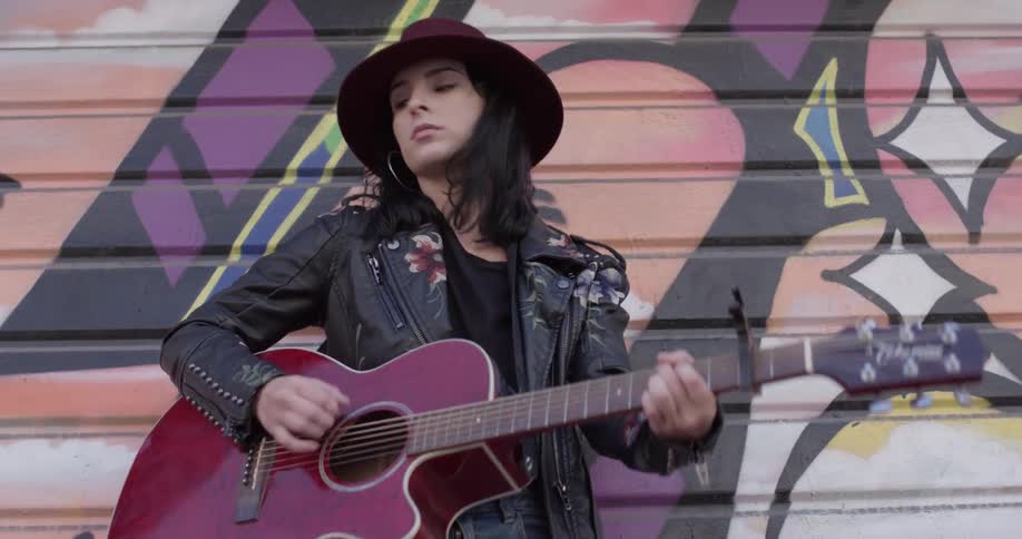 A woman playing a guitar in front of a mural on a wall