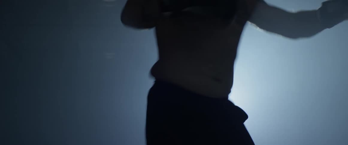 A man practices boxing in a dark gym