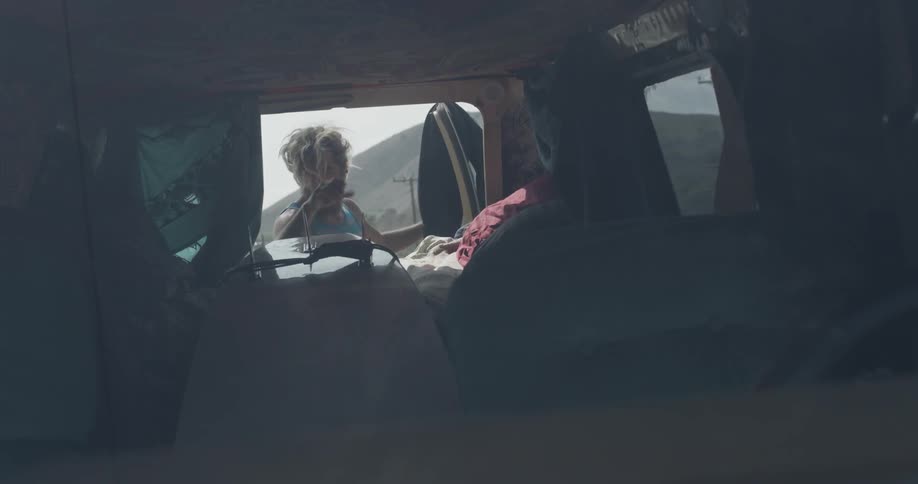 A man unloads a wetsuit and a surfboard from the back of a van