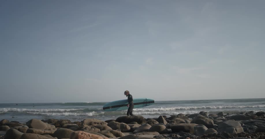 Person carries a surfboard on the beach