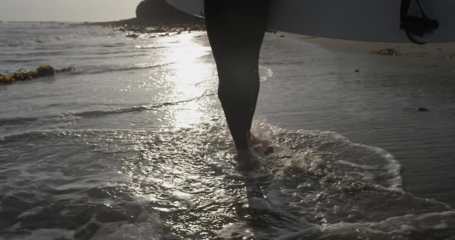 A man walking along the beach carrying a surfboard
