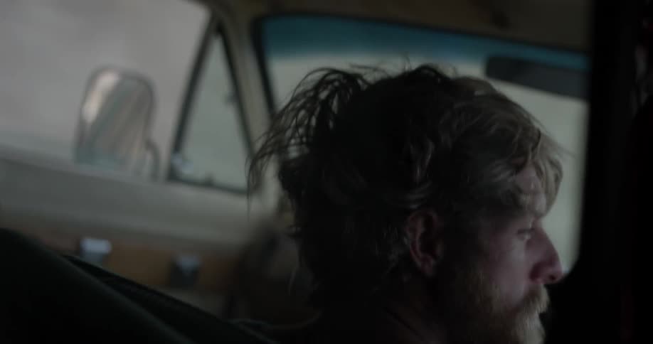 A man with scruffy hair rides in an old van