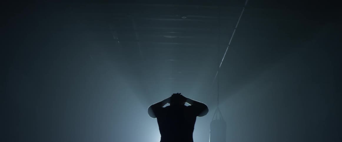 Man jumps rope in a darkened gym then walks toward a door with light streaming in