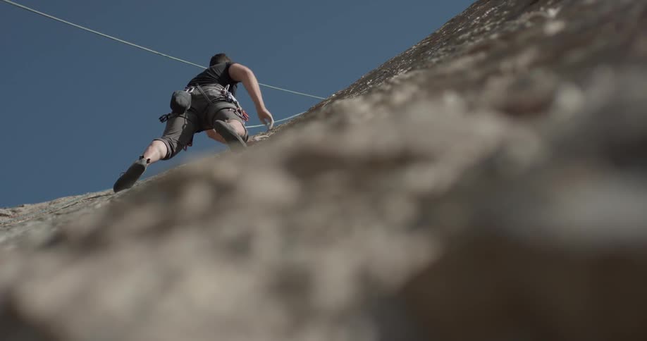 A man scales a mountain with his rock climbing equipment and dips his hand in chalk powder before continuing