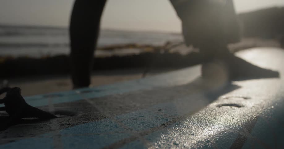 A person tethers themselves to a surfboard in front of the ocean