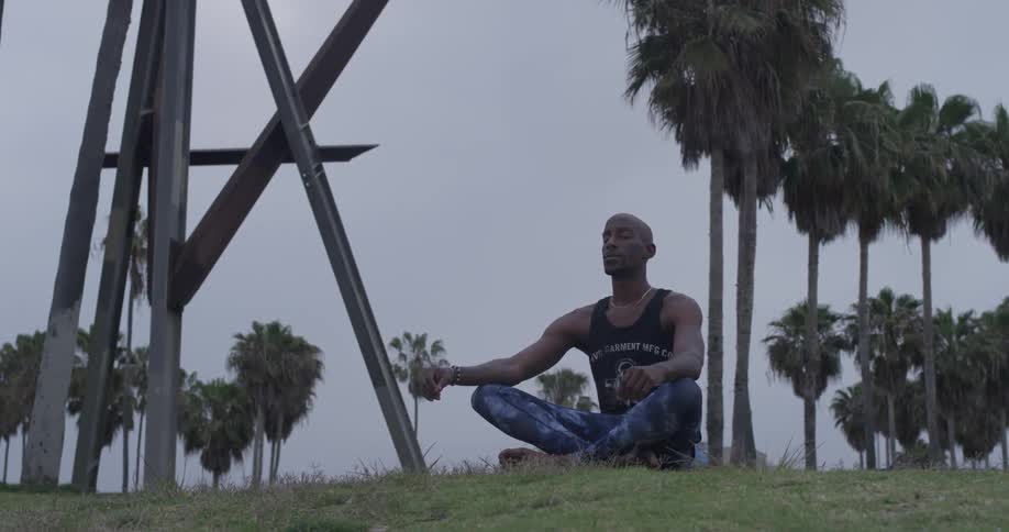 A man sits cross legged on the grass and meditates