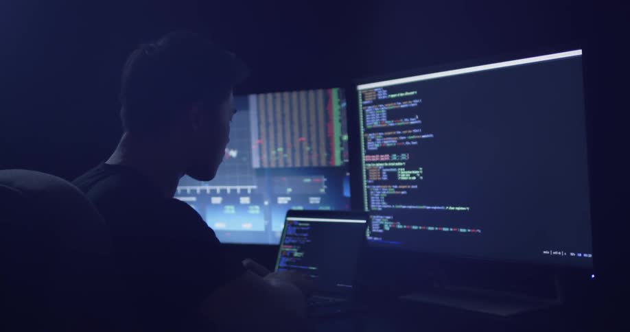 Man types on laptop at a desk with two monitors