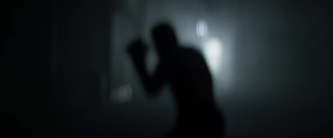 Man shadow boxes in a darkened gym as light comes in through an open door